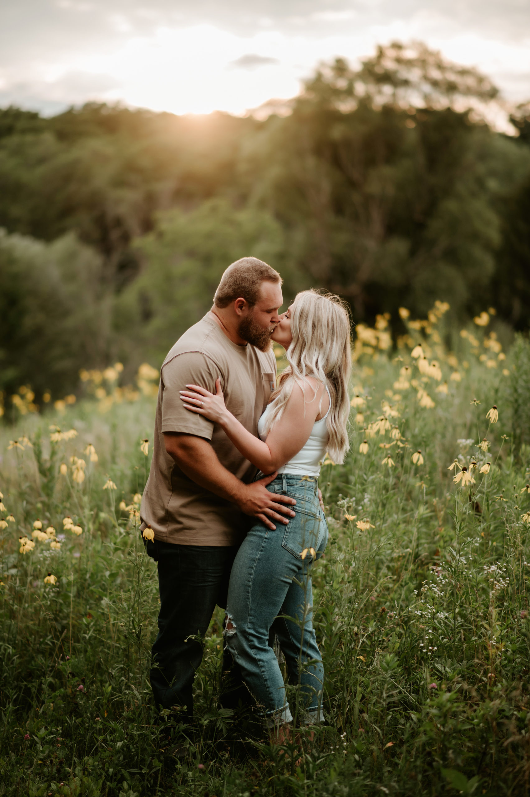 couple in jeans kissing in wildflower field in summertime